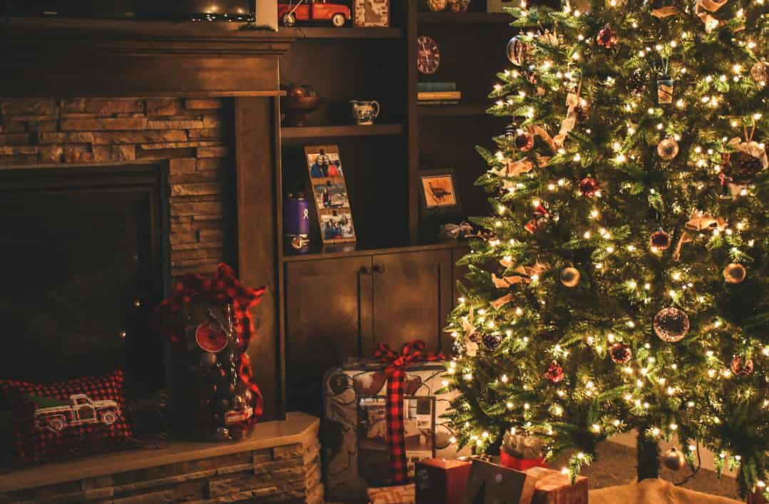 A warmly lit living room at Christmas with a decorated tree, gifts, and a fireplace