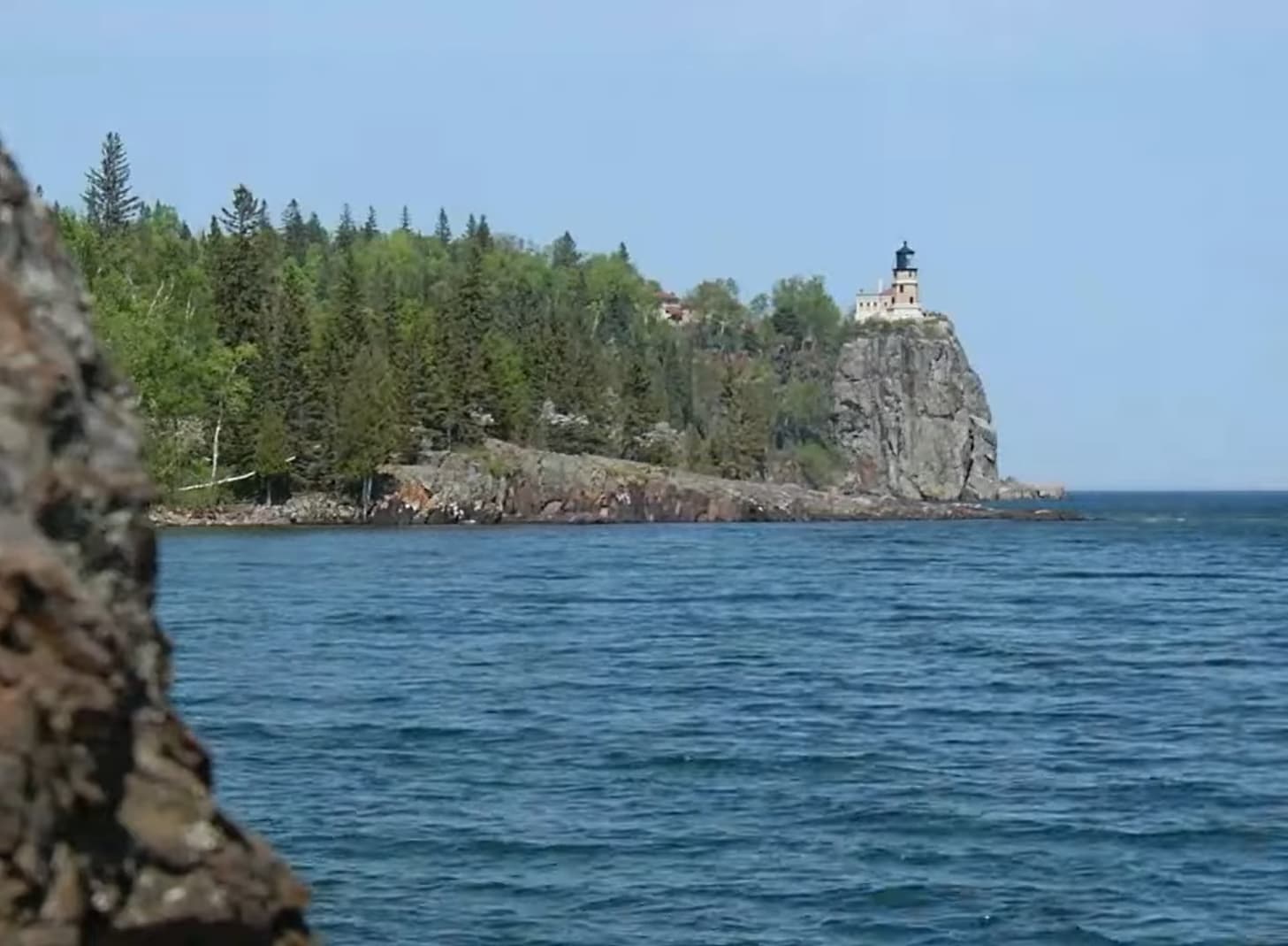 A lighthouse perched atop a steep cliff overlooking a tranquil blue lake