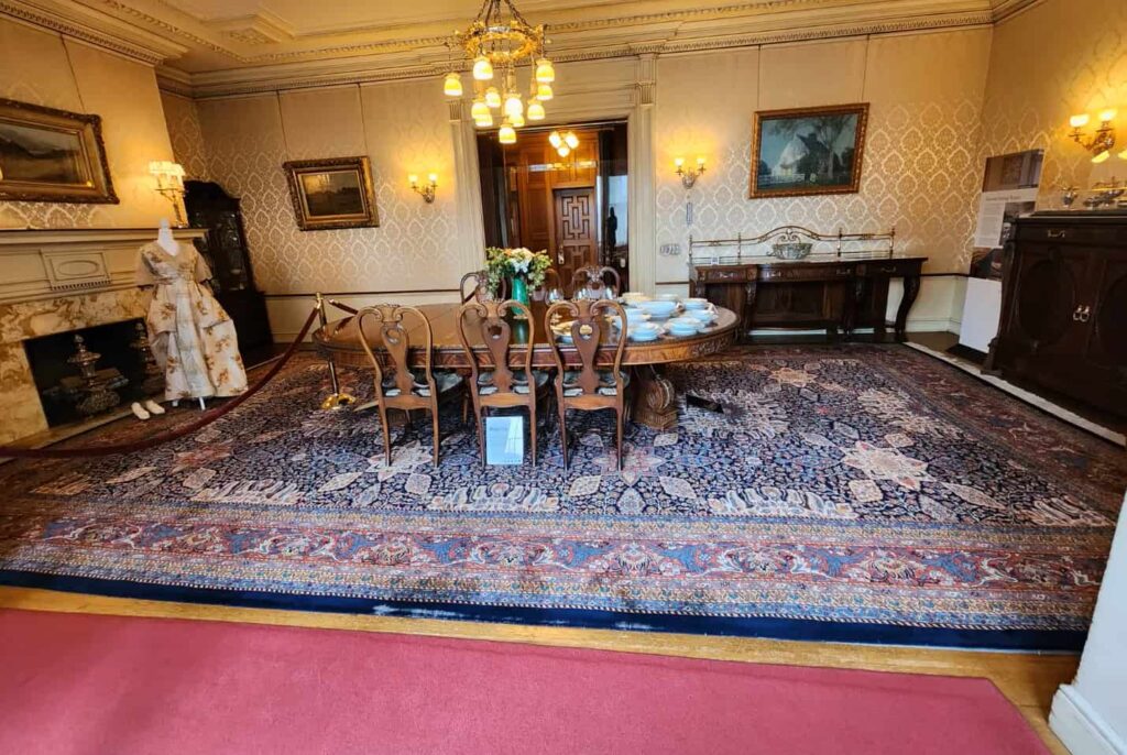 An elegant dining room with a large rug and a vintage dress on display