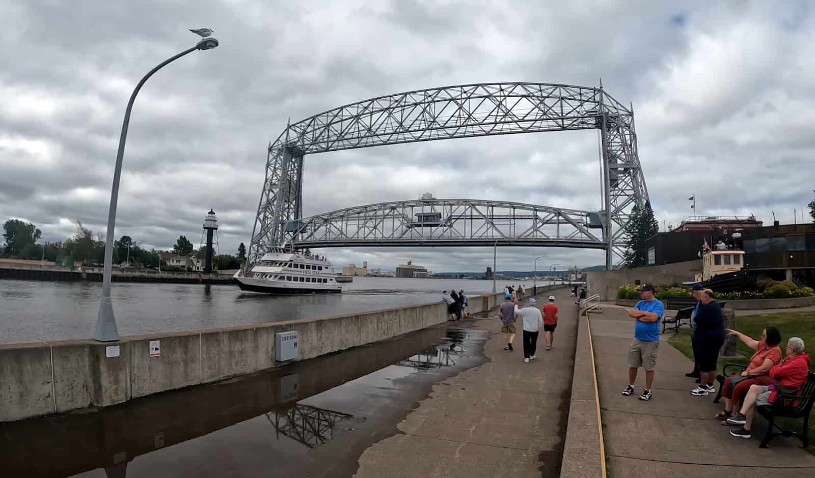People gather by Duluth's lift bridge as a boat sails underneath on a cloudy day