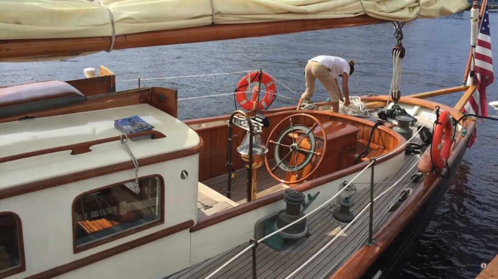A person prepares a vintage sailboat with polished wood and brass details